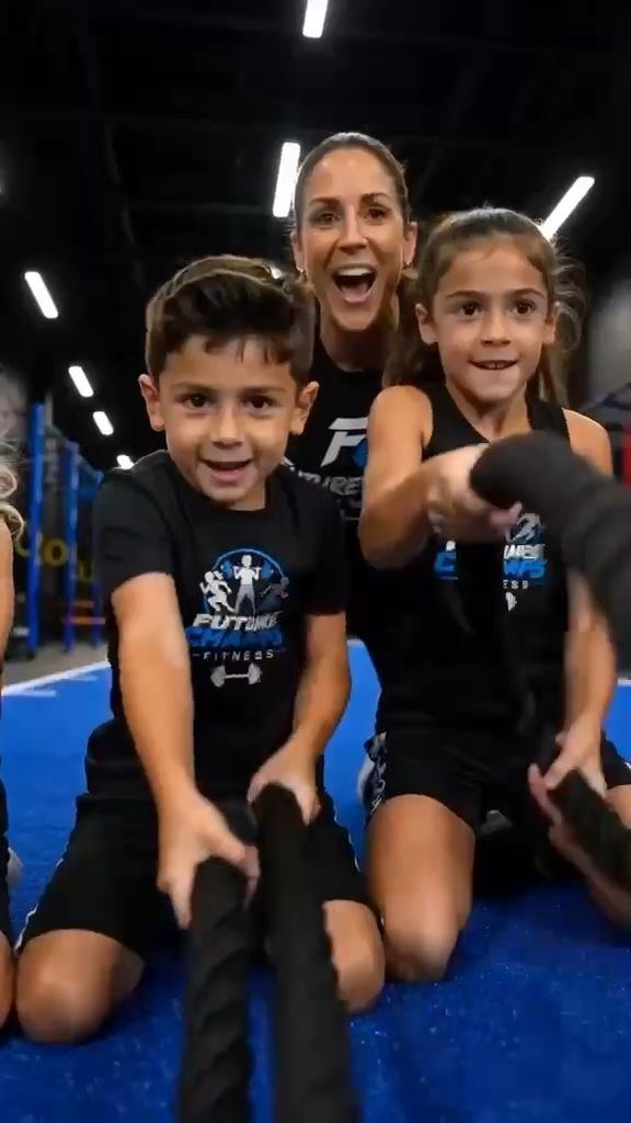 Two children pulling battle ropes with an adult cheering behind them