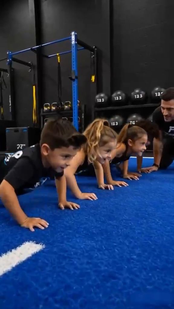 A line of children holding a push-up position on blue turf