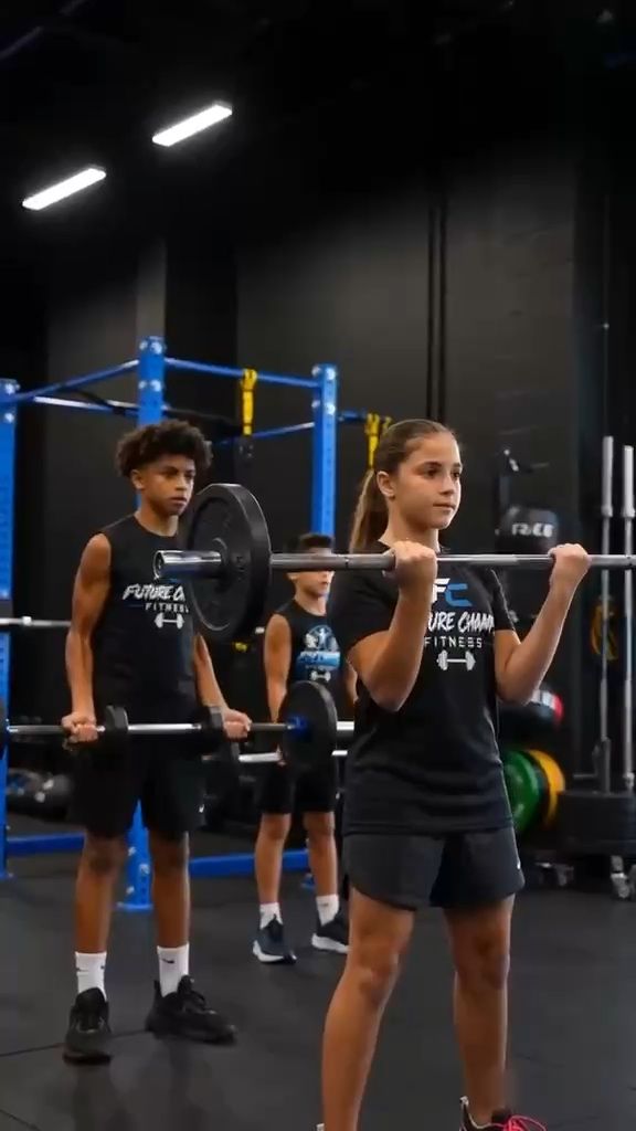 Two teenagers lifting barbells to shoulder height in a gym