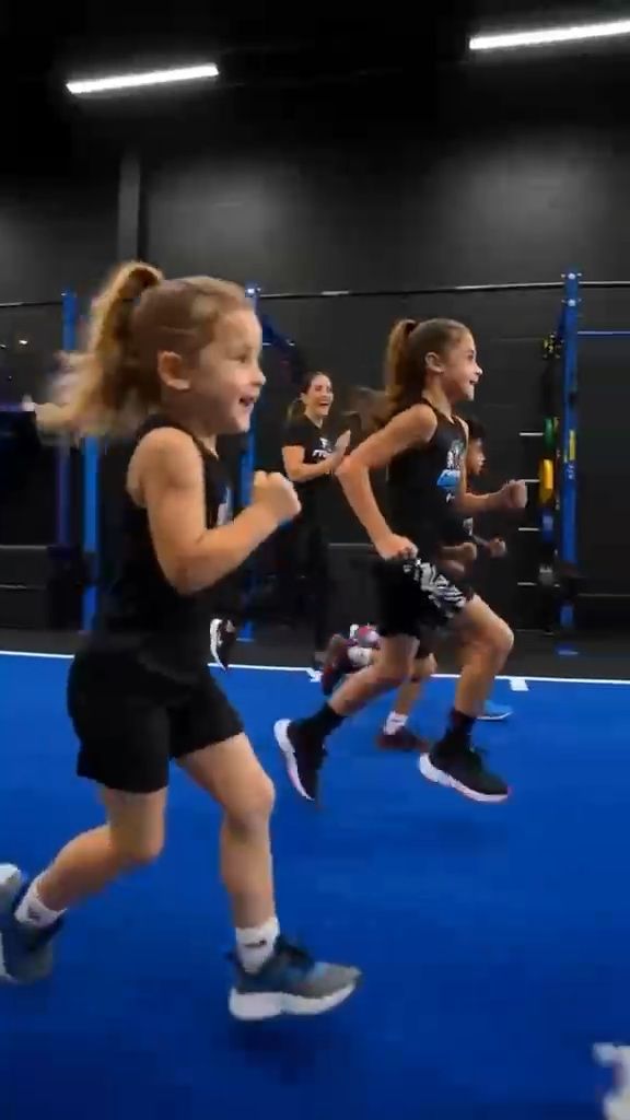 A young girl running across blue turf with other children behind her